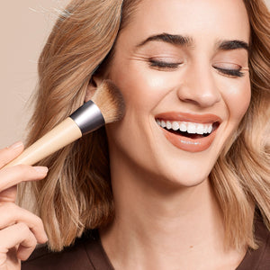 Woman smiling while using a face makeup brush near her cheek