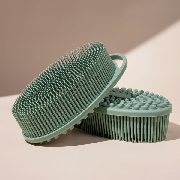 Two sage green silicone body scrubbers stacked, showing textured bristle sides