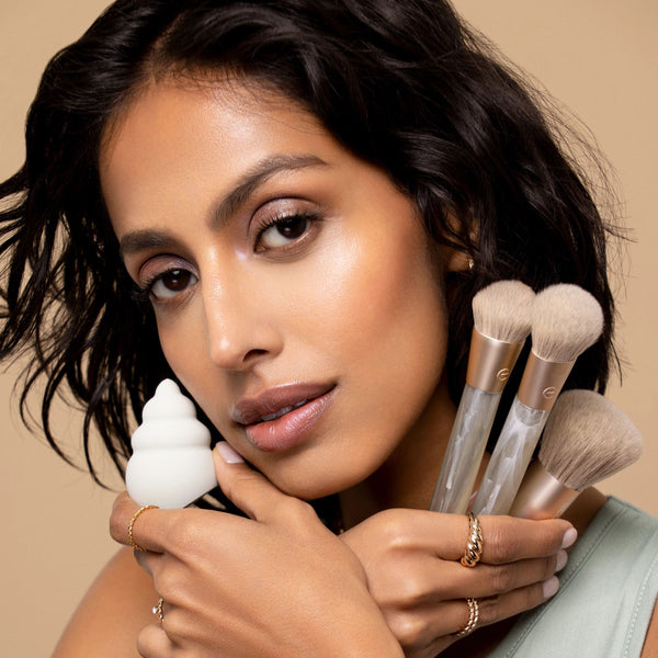 Model holding Sea Gems brushes and white sponge with soft light bristles near cheek