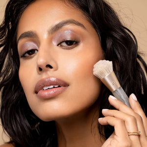 Facial makeup brush in use, holding a small Sea Gems brush with soft light bristles
