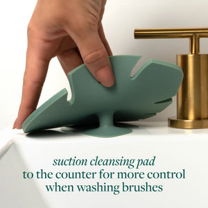 Hand pressing a green makeup brush cleansing pad against a countertop for suction