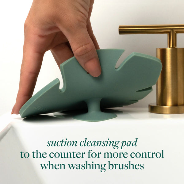 Hand pressing a green makeup brush cleansing pad against a countertop for suction