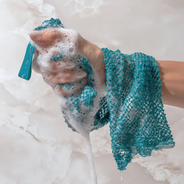 Blue-teal exfoliating bath net scrubbing a person in foamy bath water