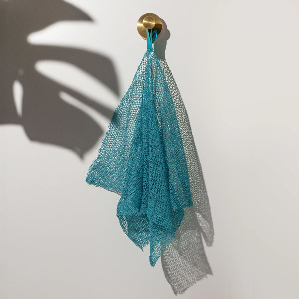 Teal exfoliating bath net hanging from a gold hook; textured mesh