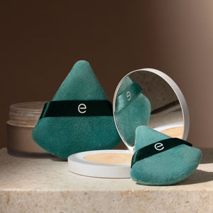 Two teal triangular powder puffs with dark green bands, one with open mirror