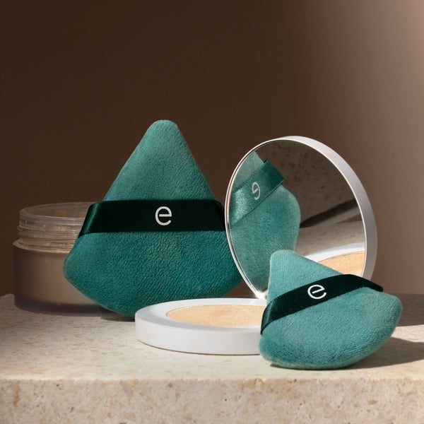 Two teal triangular powder puffs with dark green bands, one with open mirror