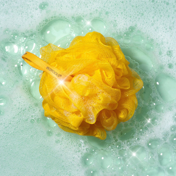 Yellow delicate EcoPouf bath sponge floating in water with bubbles