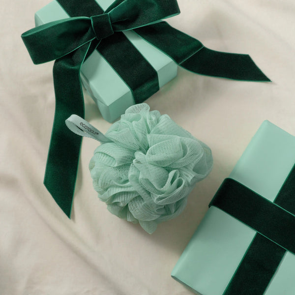 Delicate pouf: mint green mesh bath scrub ball with dark green ribbon, gift box nearby