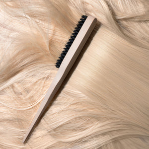 Slick back brush angled on hair strands with cream handle and black bristle row