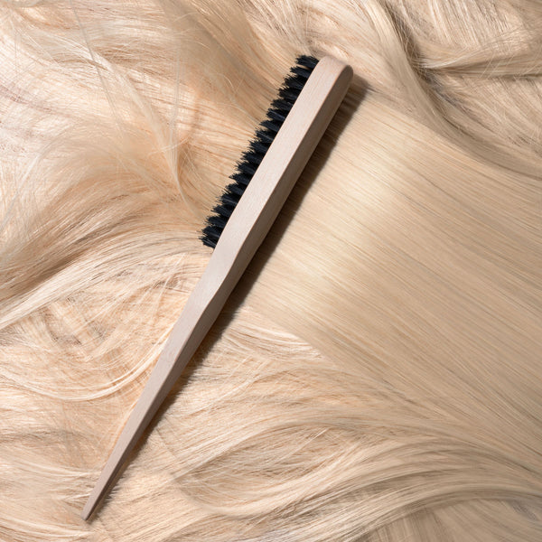 Slick back brush angled on hair strands with cream handle and black bristle row