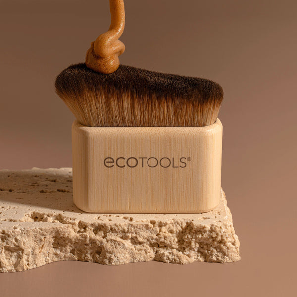Self-tan blending brush with dark bristles above self-tan powder on a textured surface