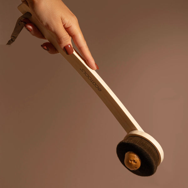 Hand holding wooden self-tan applicator with round brush head at bottom