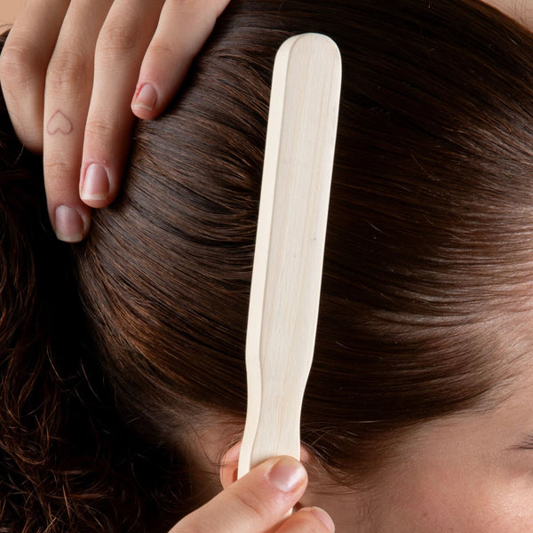 Wooden paddle slick back brush held against hair, light bristles