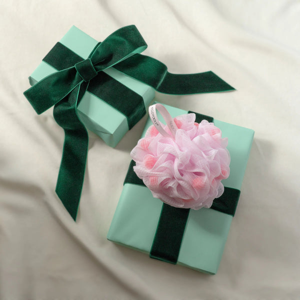 Pink mesh bath pouf on aqua gift box with dark green ribbon bow