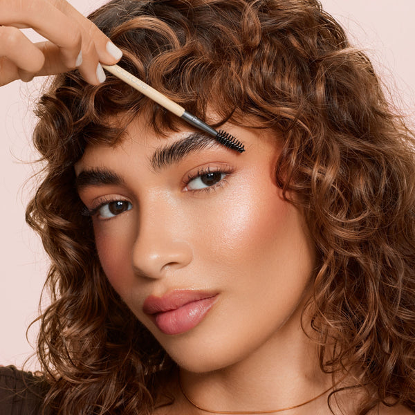 Eyebrow brush duo held near eyebrow, featuring black spoolie brush end