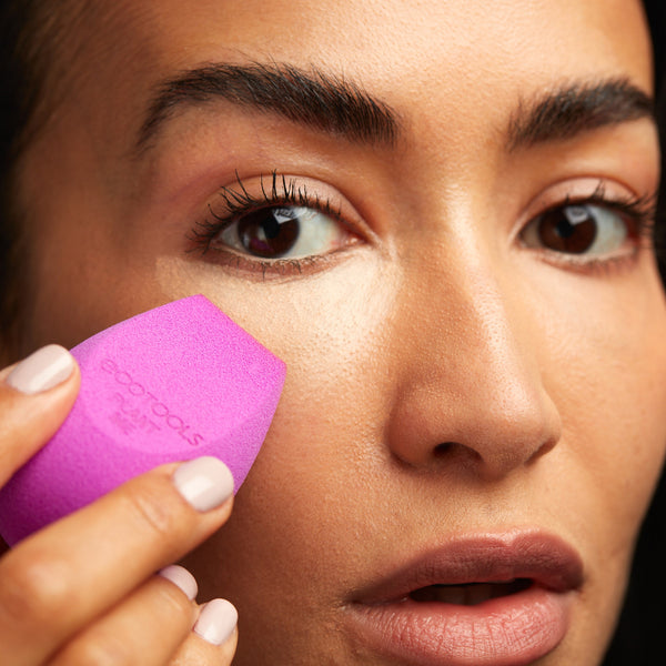 Purple makeup sponge pressed to skin for blending, with ecotools logo visible