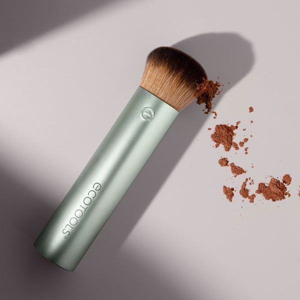 Powder makeup brush with teal metal handle and brown bristles, with scattered powder