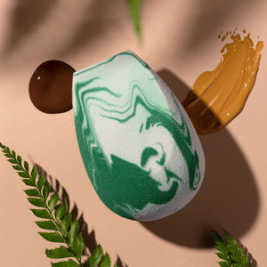 Teardrop blending sponge held above skin, showing green and white swirled foam surface.