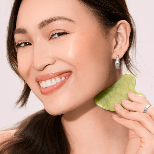 Green jade gua sha pressed along jawline and neck, heart-shaped stone