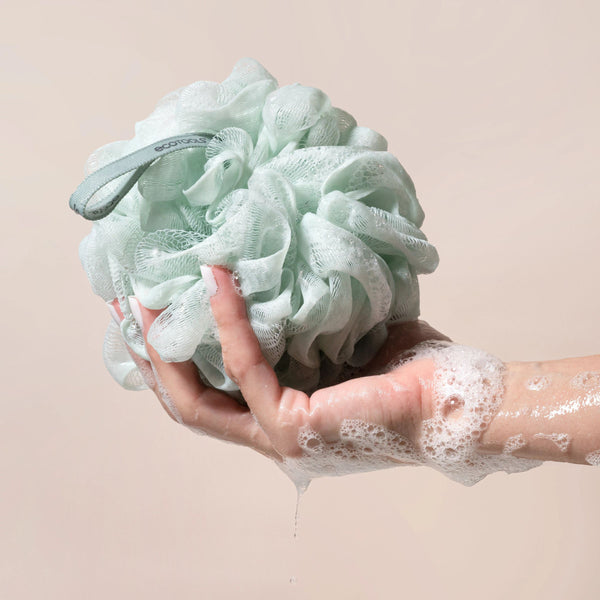 Green recycled mesh bath pouf held in hand, with hanging loop