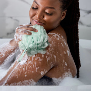 Green recycled mesh bath pouf for gentle cleansing, held near the body