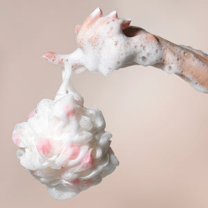 Bath sponge pouf in hands, covered with white lather foam