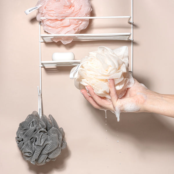 White mesh flower loofah bath sponge held in hand, with gray loofah nearby