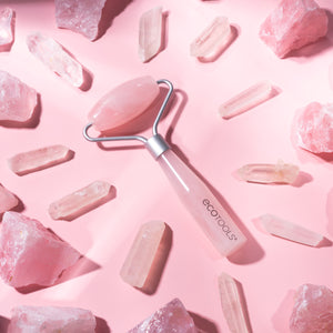 Mini rose quartz facial roller on pink crystal pieces, with a silver frame and pink handle.
