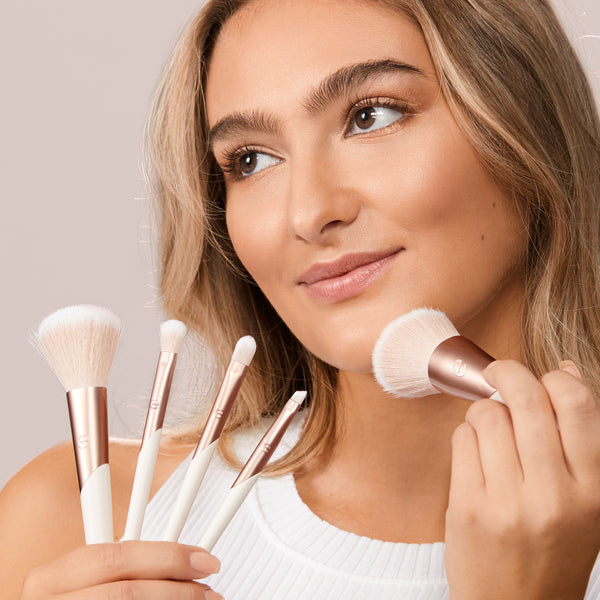 Woman using a fluffy makeup brush from the Luxe Collection set; other brushes in view
