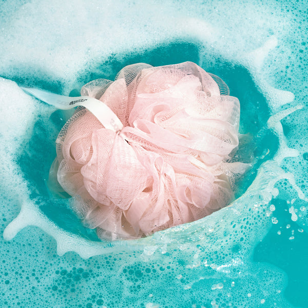 Pink EcoPouf bath sponge floating in foamy water