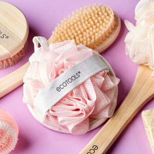 Pink loofah cleansing pad with gray ecotools strap, round puff, and hanging loop.