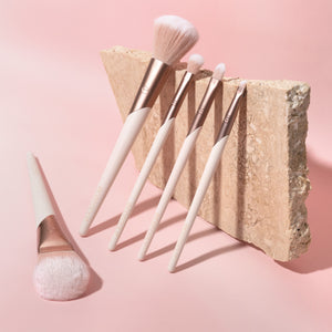 ECOTOOLS makeup brush set with light bristles and white handles, arranged on a stone backdrop