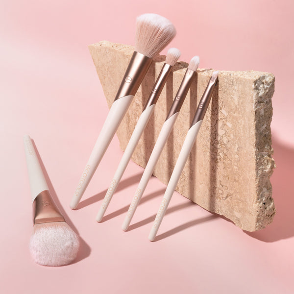 ECOTOOLS makeup brush set with light bristles and white handles, arranged on a stone backdrop